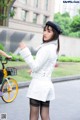 A woman in a white jacket and black hat standing next to a bike.