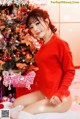 A woman in a red sweater sitting in front of a Christmas tree.