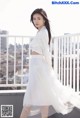 A woman in a white shirt and skirt standing on a balcony.