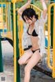 A woman in a black bikini sitting on a playground.