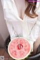 A woman in a white shirt holding a slice of watermelon.