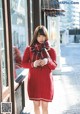 A woman in a red sweater dress is standing outside of a store.